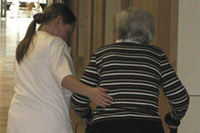 Eine Pflegerin hilft einer Bewohnerin im Pflegeheim über den Flur.