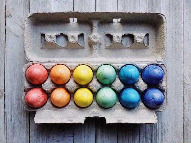 Blick von oben auf bunte Ostereier im Regenbogenfarbenspektrum in einem offenen Eierkarton.